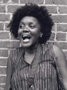 Alicia Bunyan-Sampson smiling with mouth open against brick wall.