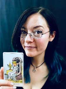 Carrie Jenkins wearing glasses and holding a tarot card.