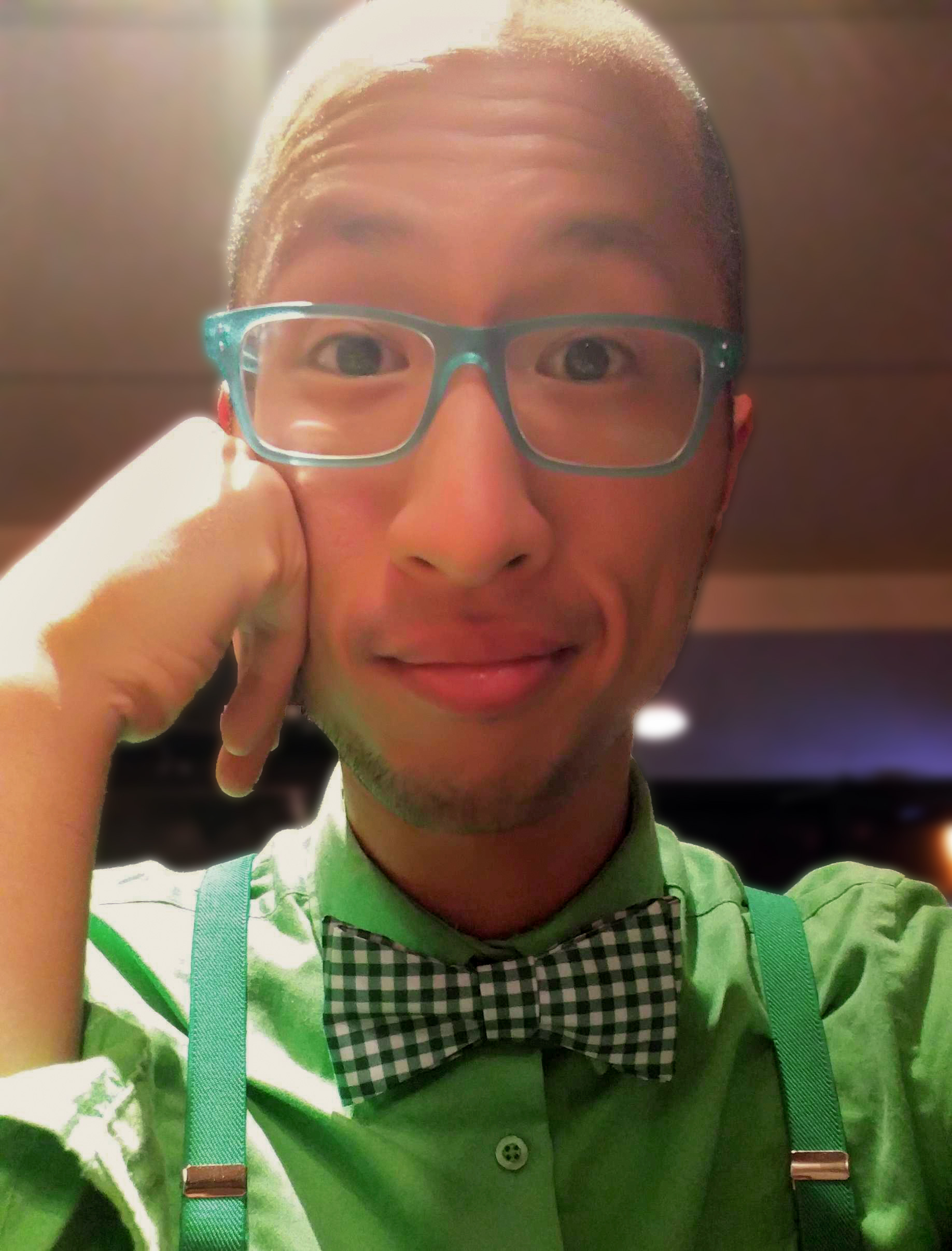 Asian man wearing glasses and resting his head on one hand in a green shirt and green bow tie.
